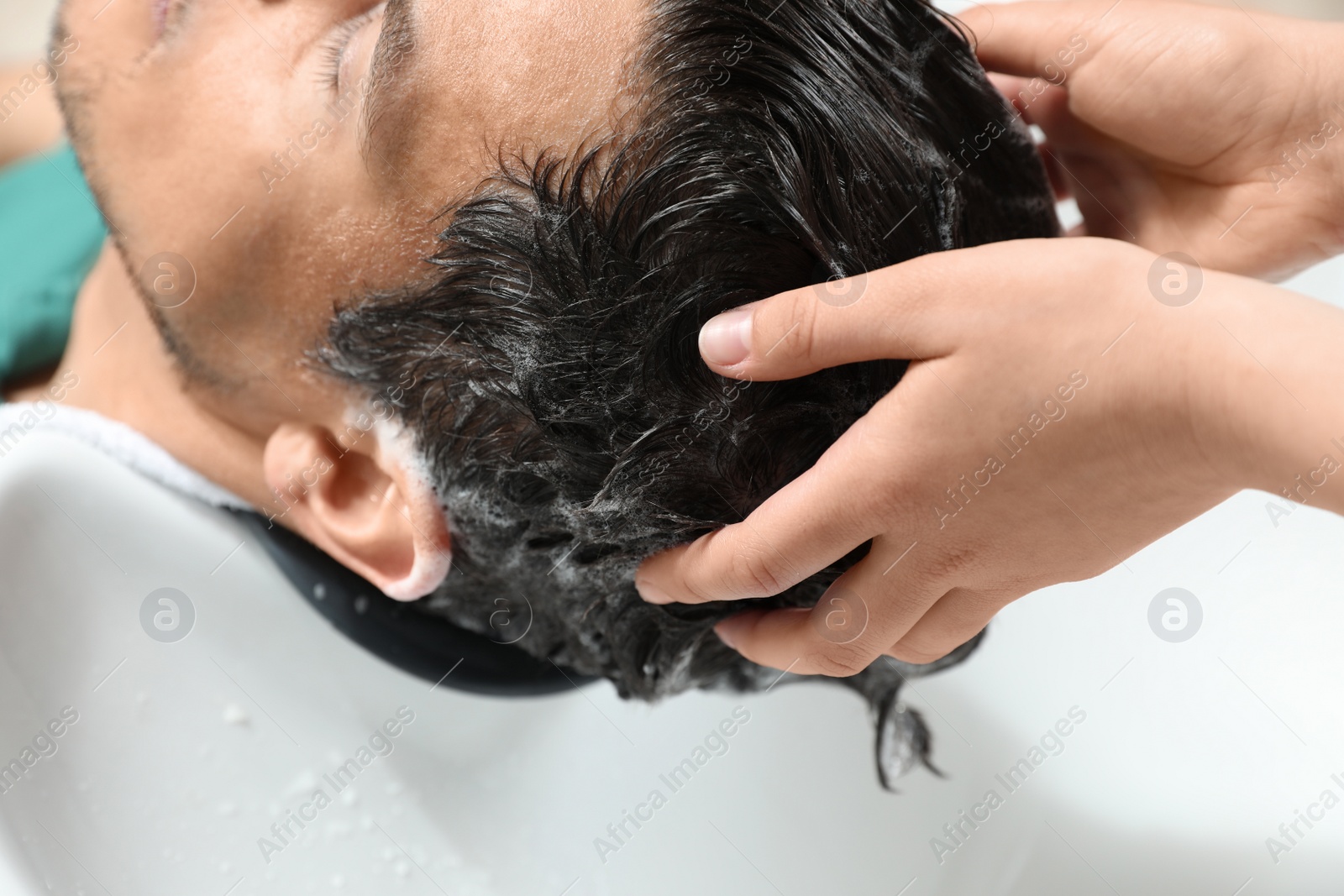 Photo of Stylist washing client's hair at sink in beauty salon, closeup