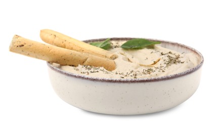 Photo of Bowl of delicious hummus with grissini sticks, basil leaves and spices isolated on white