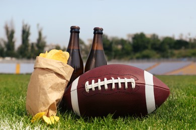 Photo of American football ball with beer and chips on green field grass in stadium