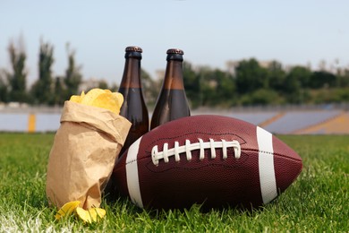 American football ball with beer and chips on green field grass in stadium