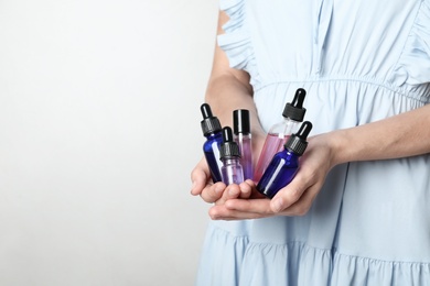 Photo of Woman holding bottles of essential oil on light background, closeup. Space for text