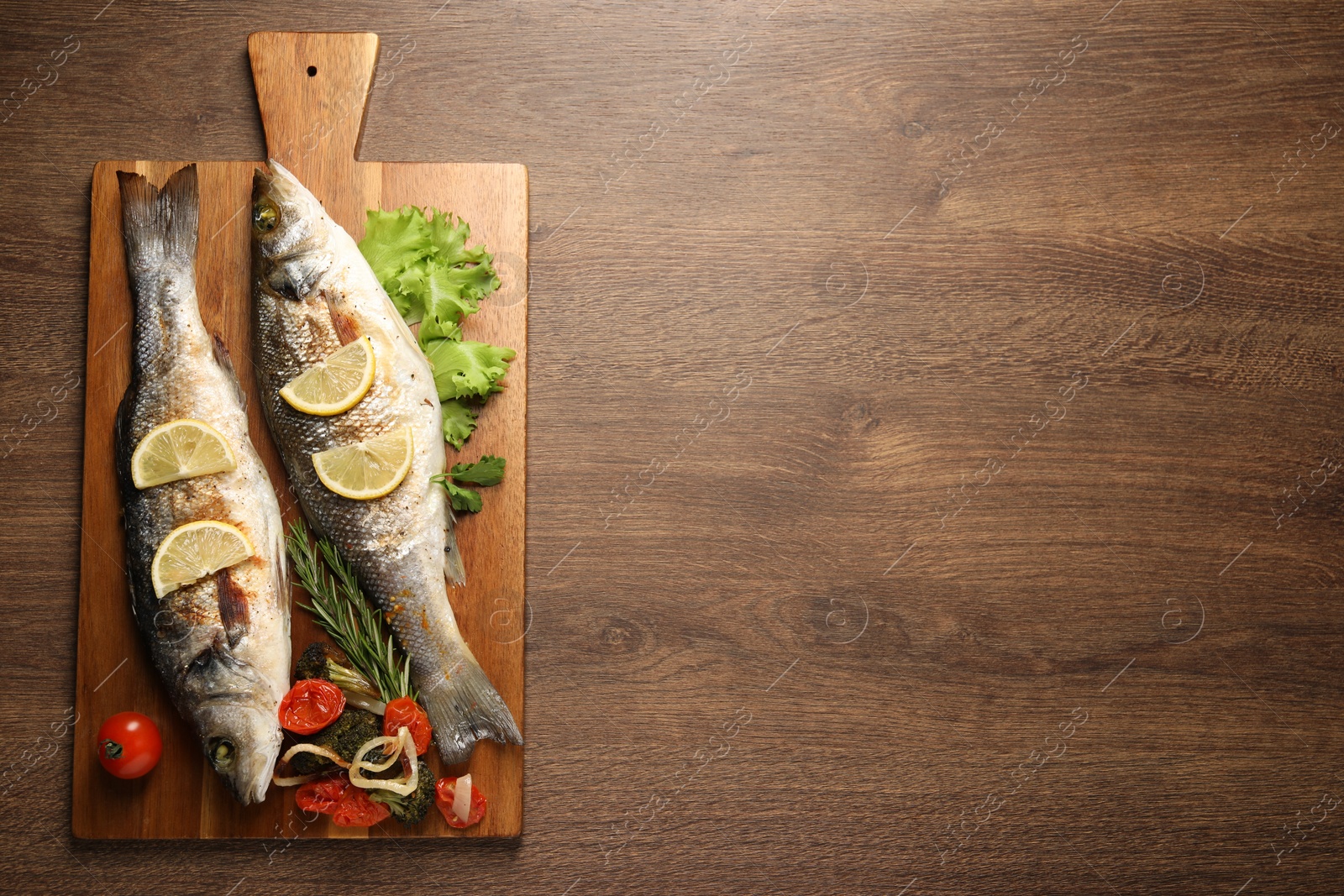 Photo of Delicious baked fish and vegetables on wooden table, top view. Space for text