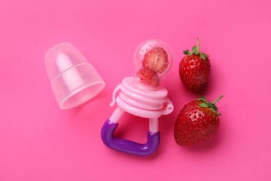 Photo of Nibbler with fresh strawberries on pink background, flat lay. Baby feeder