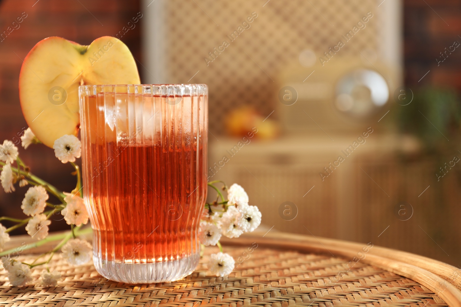 Photo of Glass of tasty cider and flowers on wicker table in room, space for text. Relax at home