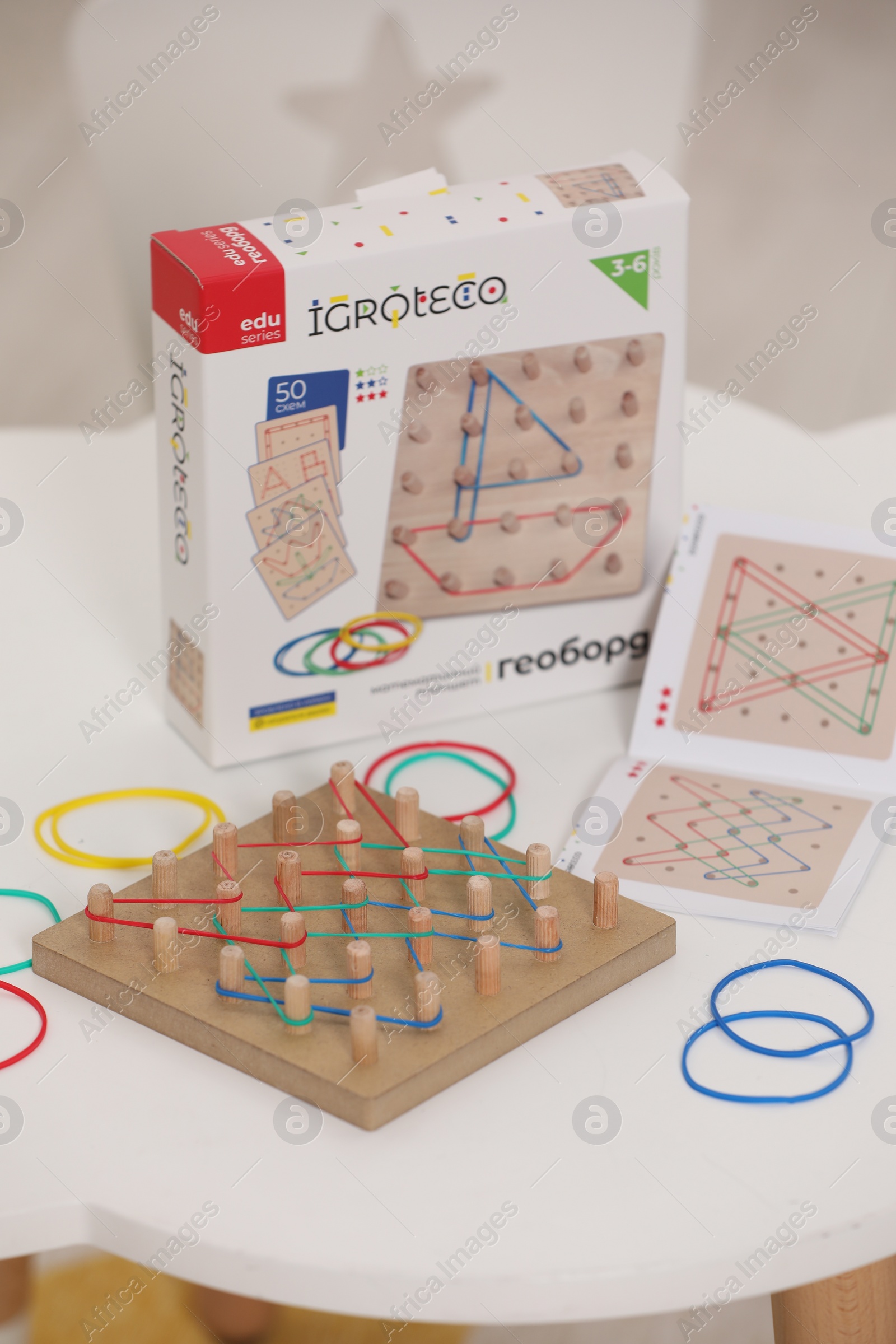 Photo of Wooden geoboard with rubber bands on white table indoors. Educational toy for motor skills development