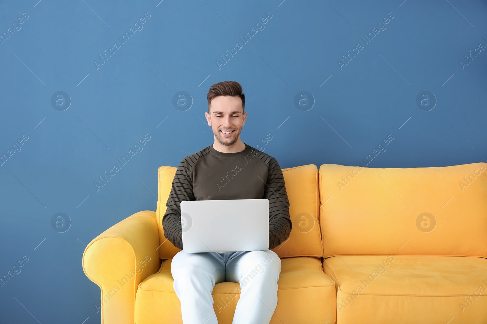 Photo of Handsome young man with laptop sitting on sofa, indoors