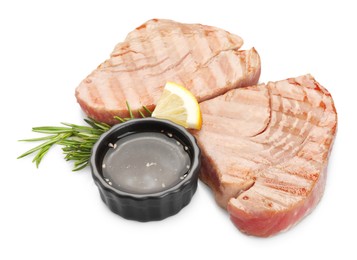 Photo of Delicious tuna steaks with sauce, lemon and rosemary isolated on white