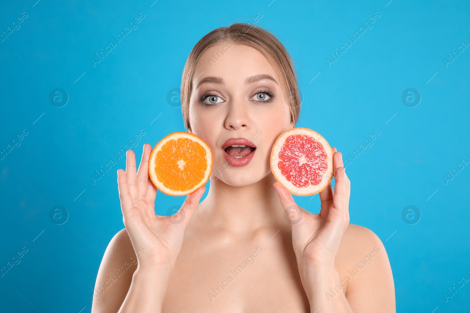 Photo of Emotional young woman with cut grapefruit and orange on blue background. Vitamin rich food