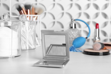 Photo of Stylish pocket mirror and cosmetic products on white table