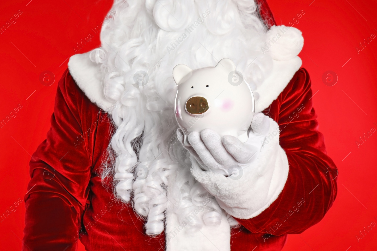 Photo of Santa Claus holding piggy bank on red background, closeup