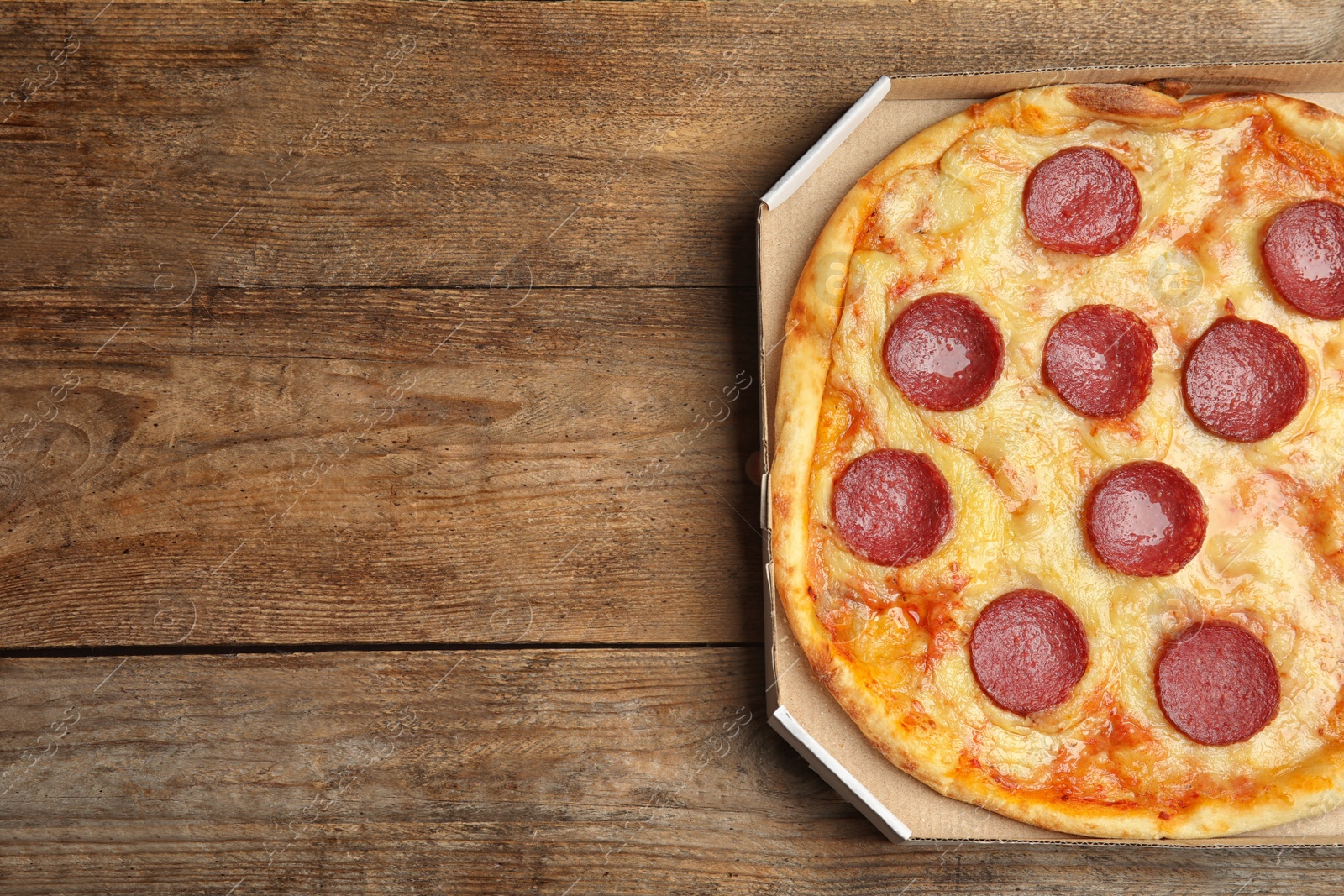 Photo of Tasty pepperoni pizza in cardboard box on wooden table, top view. Space for text