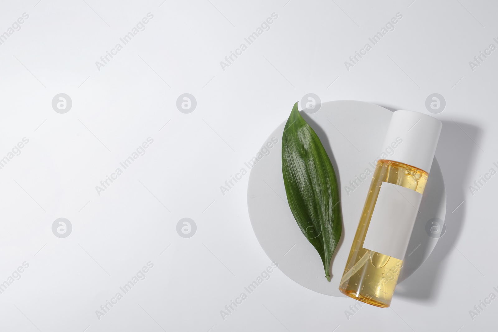 Photo of Bottle with cosmetic oil and green leaf on white background, top view. Space for text