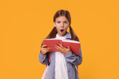 Photo of Emotional schoolgirl with open book on orange background