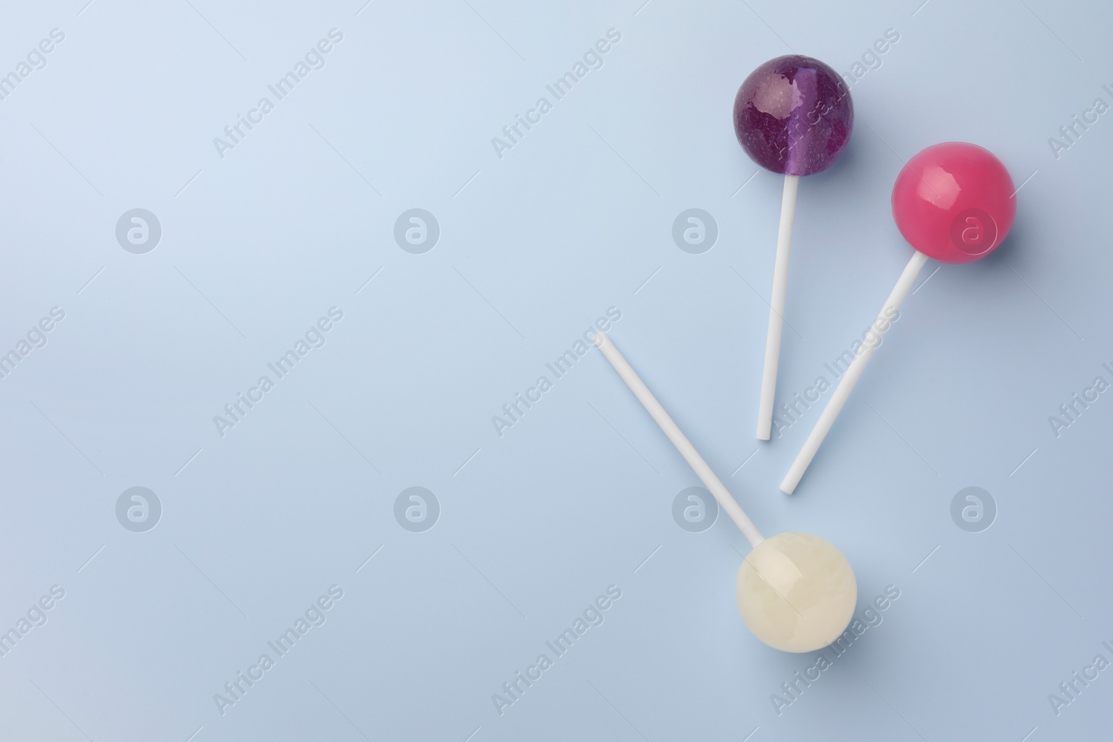 Photo of Tasty lollipops on light blue background, flat lay. Space for text