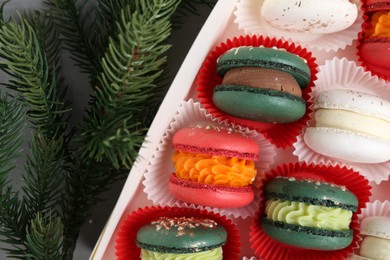 Different tasty Christmas macarons in box and fir branches on table, top view