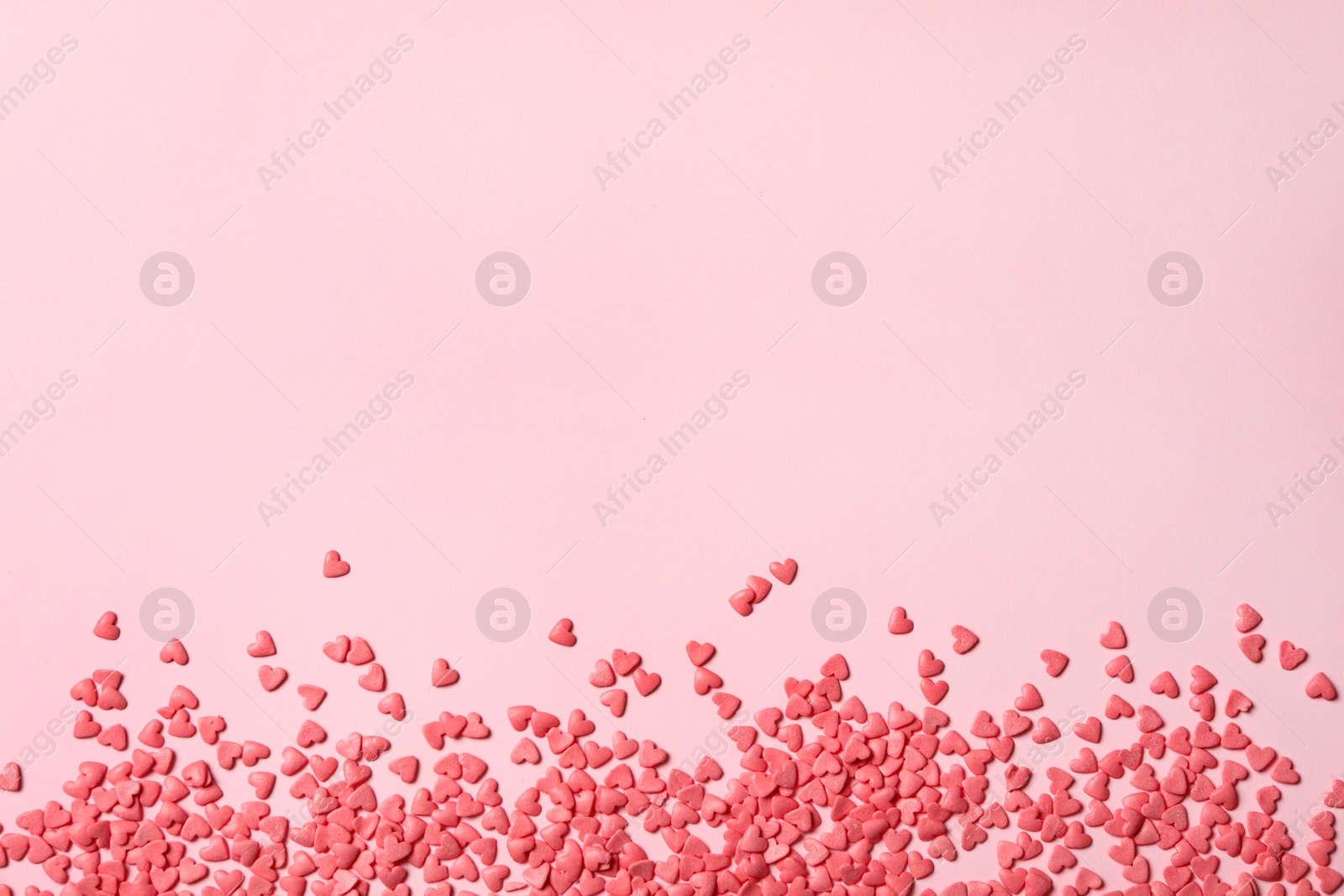 Photo of Heart shaped sprinkles on pink background, flat lay. Space for text