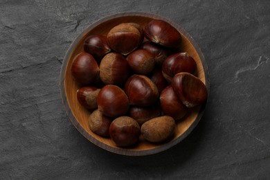 Photo of Roasted edible sweet chestnuts in bowl on grey textured table, top view