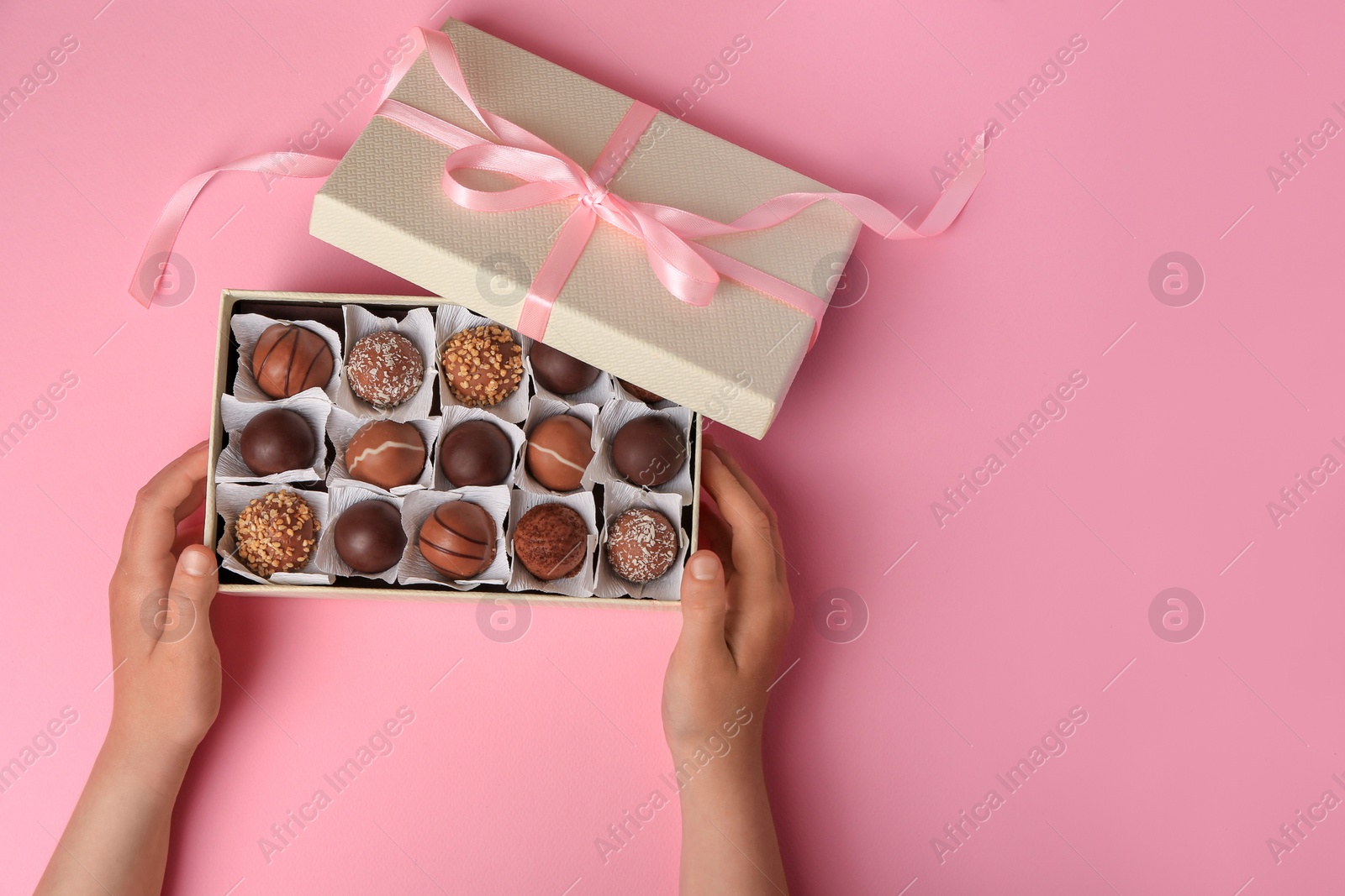 Photo of Child with box of delicious chocolate candies on pink background, top view. Space for text