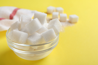 Photo of Refined sugar cubes in glass bowl on yellow background