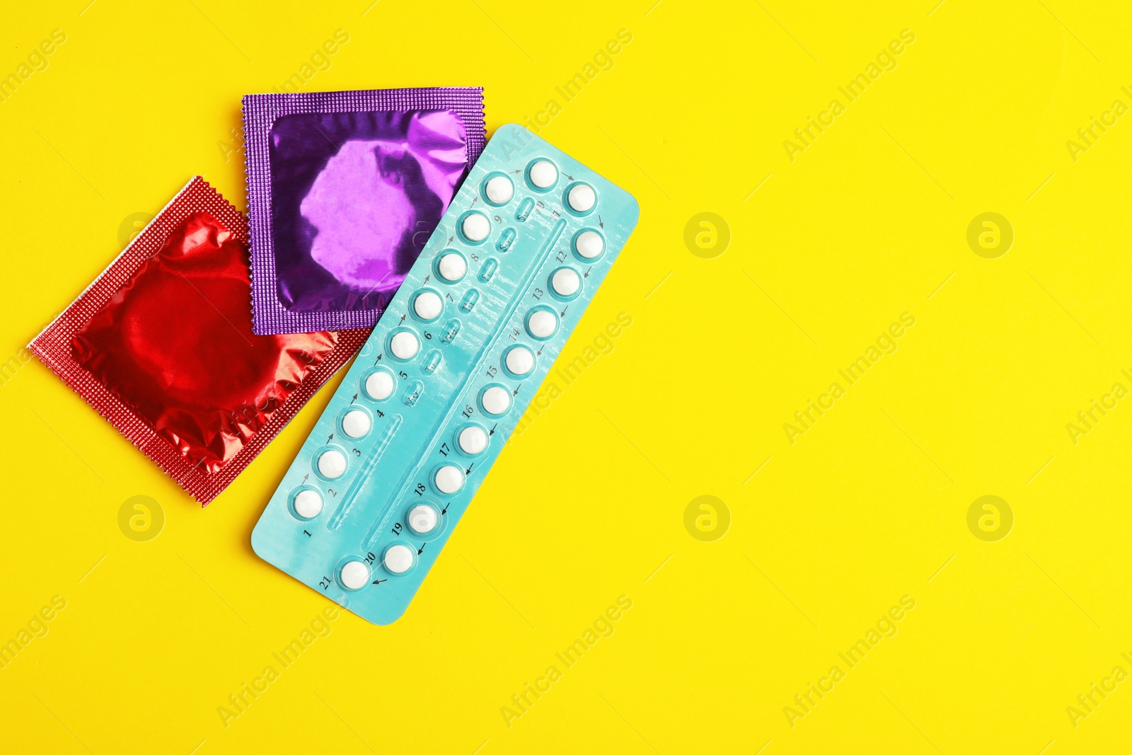 Photo of Condoms and birth control pills on yellow background, flat lay with space for text. Safe sex concept