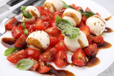 Photo of Tasty salad Caprese with tomatoes, mozzarella balls, basil and balsamic vinegar on plate, closeup