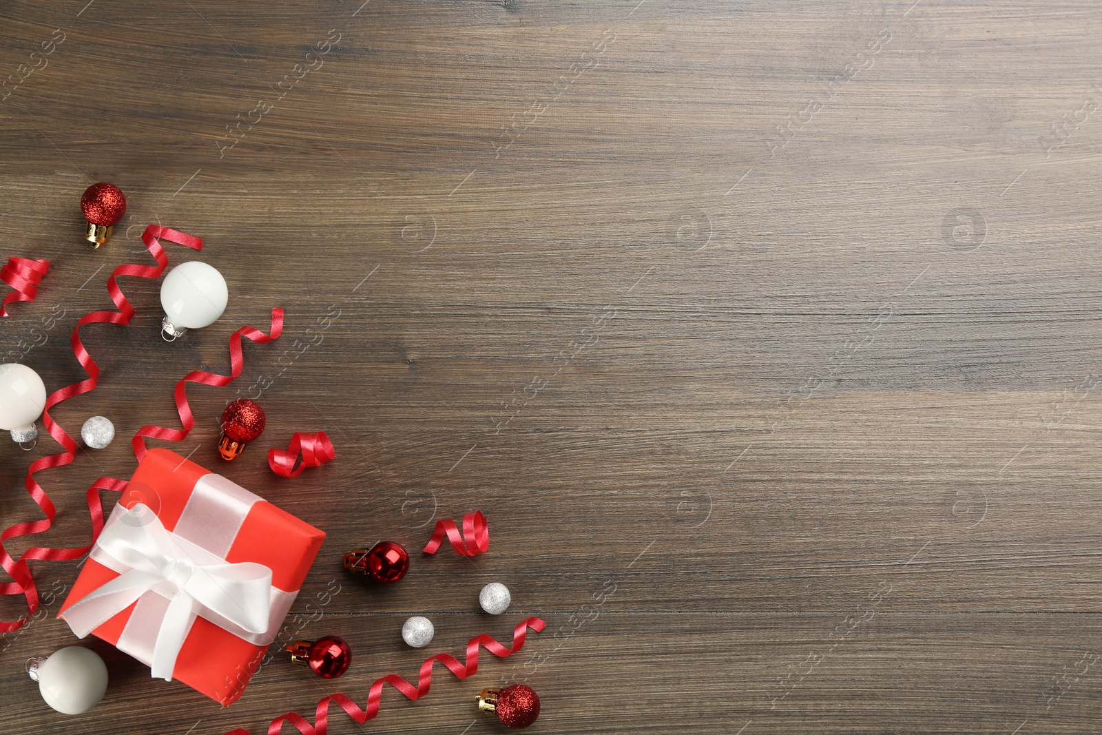 Photo of Red serpentine streamers, Christmas balls and gift box on wooden background, flat lay. Space for text