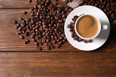 Cup of hot aromatic coffee and roasted beans on wooden table, flat lay