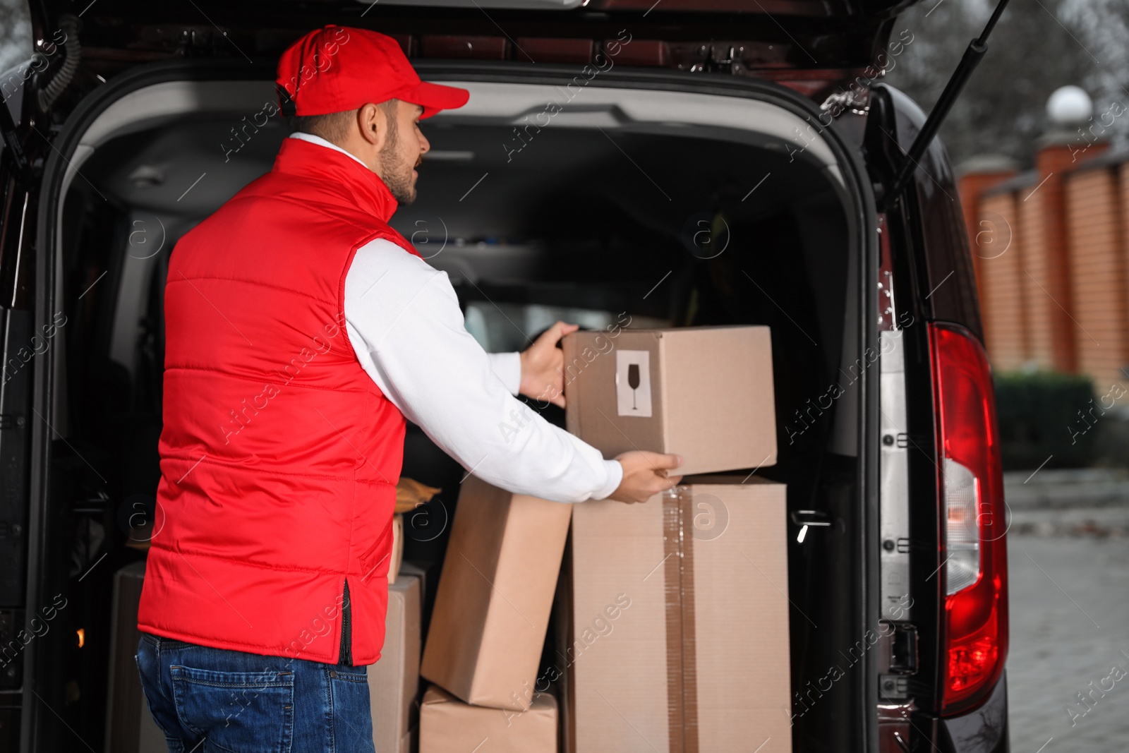 Photo of Deliveryman in uniform taking parcel from van outdoors