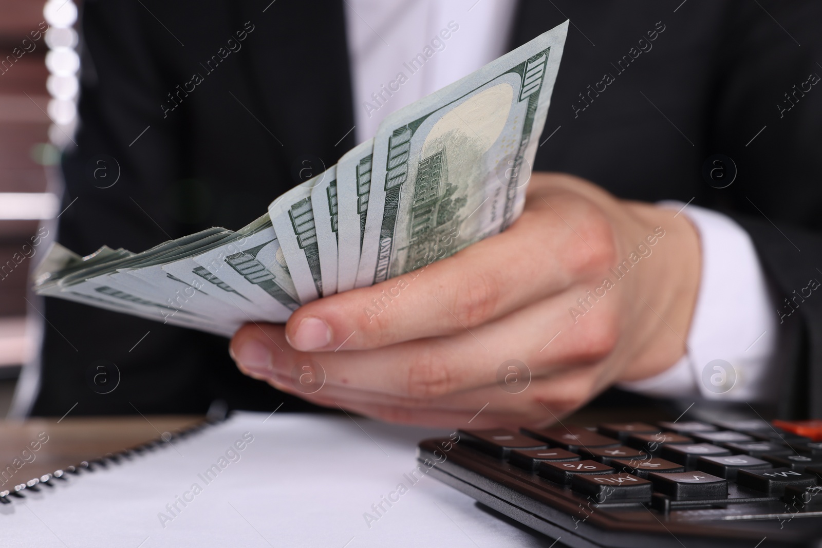 Photo of Money exchange. Man holding dollar banknotes at wooden table, closeup