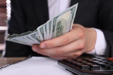 Photo of Money exchange. Man holding dollar banknotes at wooden table, closeup
