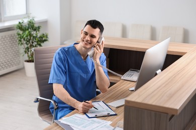 Photo of Smiling medical assistant talking by phone at hospital reception