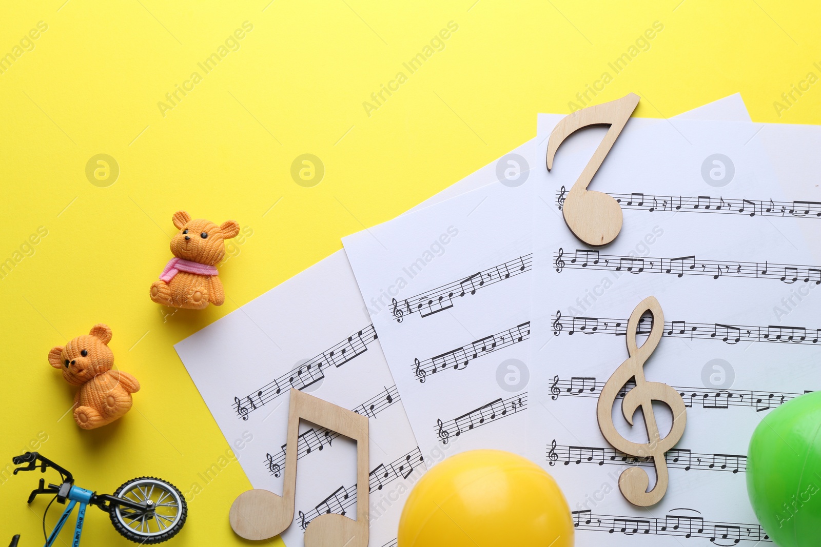 Photo of Baby songs. Music sheets, wooden notes and different toys on yellow background, flat lay