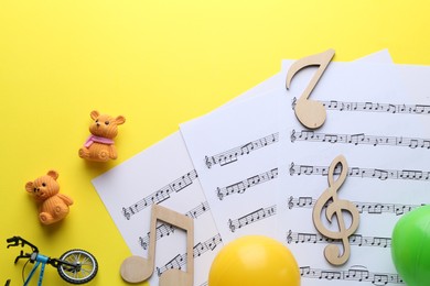 Baby songs. Music sheets, wooden notes and different toys on yellow background, flat lay