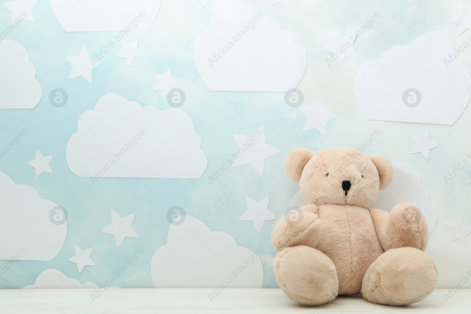 Photo of Teddy bear on white wooden table near wall with blue sky, space for text. Baby room interior