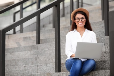 Photo of Beautiful woman with laptop sitting on stairs outdoors