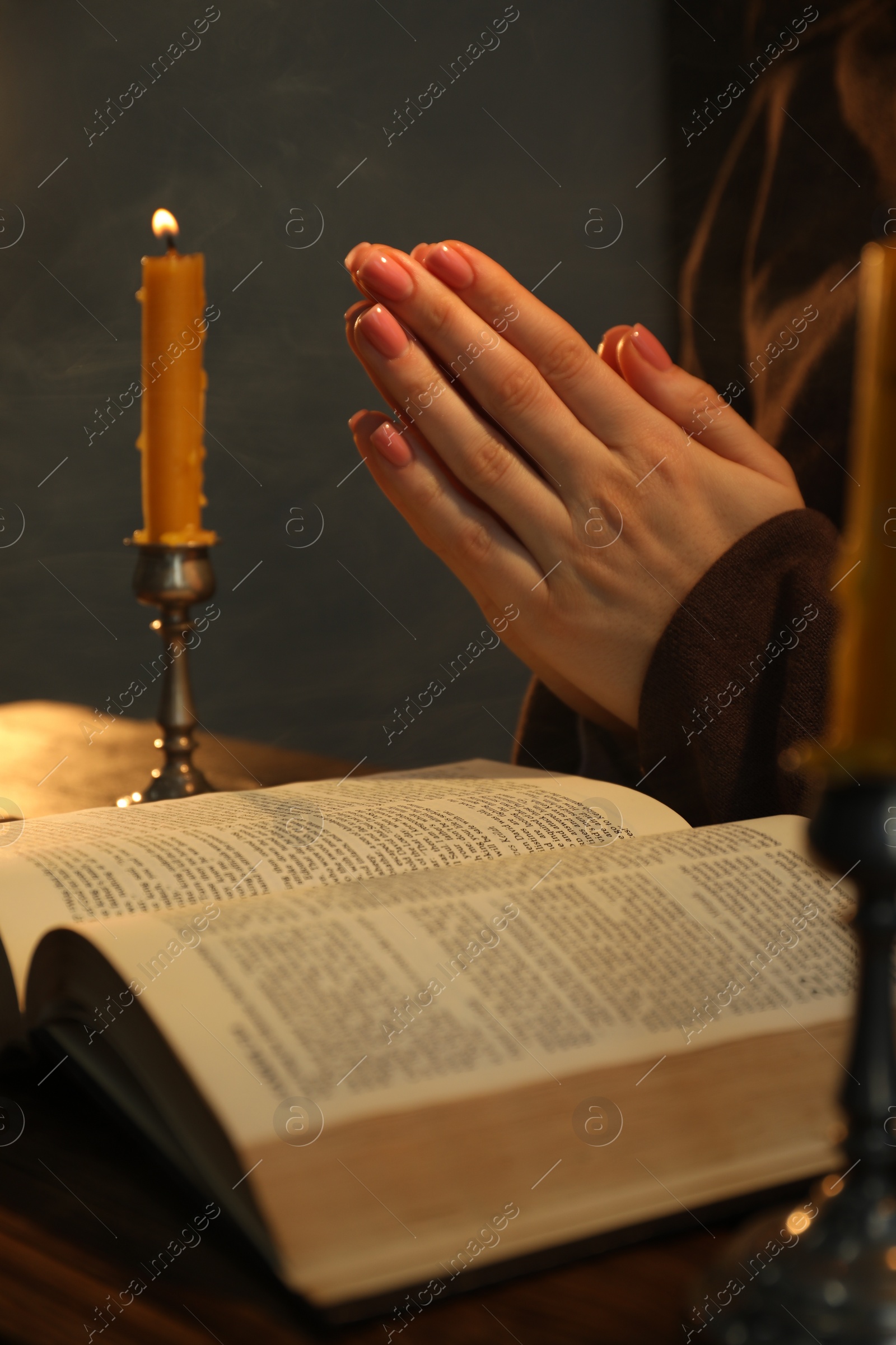 Photo of Woman praying at table with burning candle and Bible, closeup