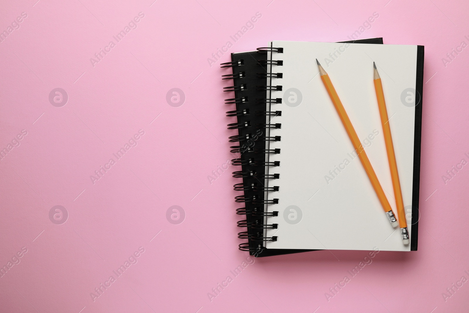 Photo of Notebooks and pencils on pale pink background, top view. Space for text