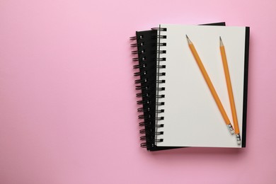 Notebooks and pencils on pale pink background, top view. Space for text