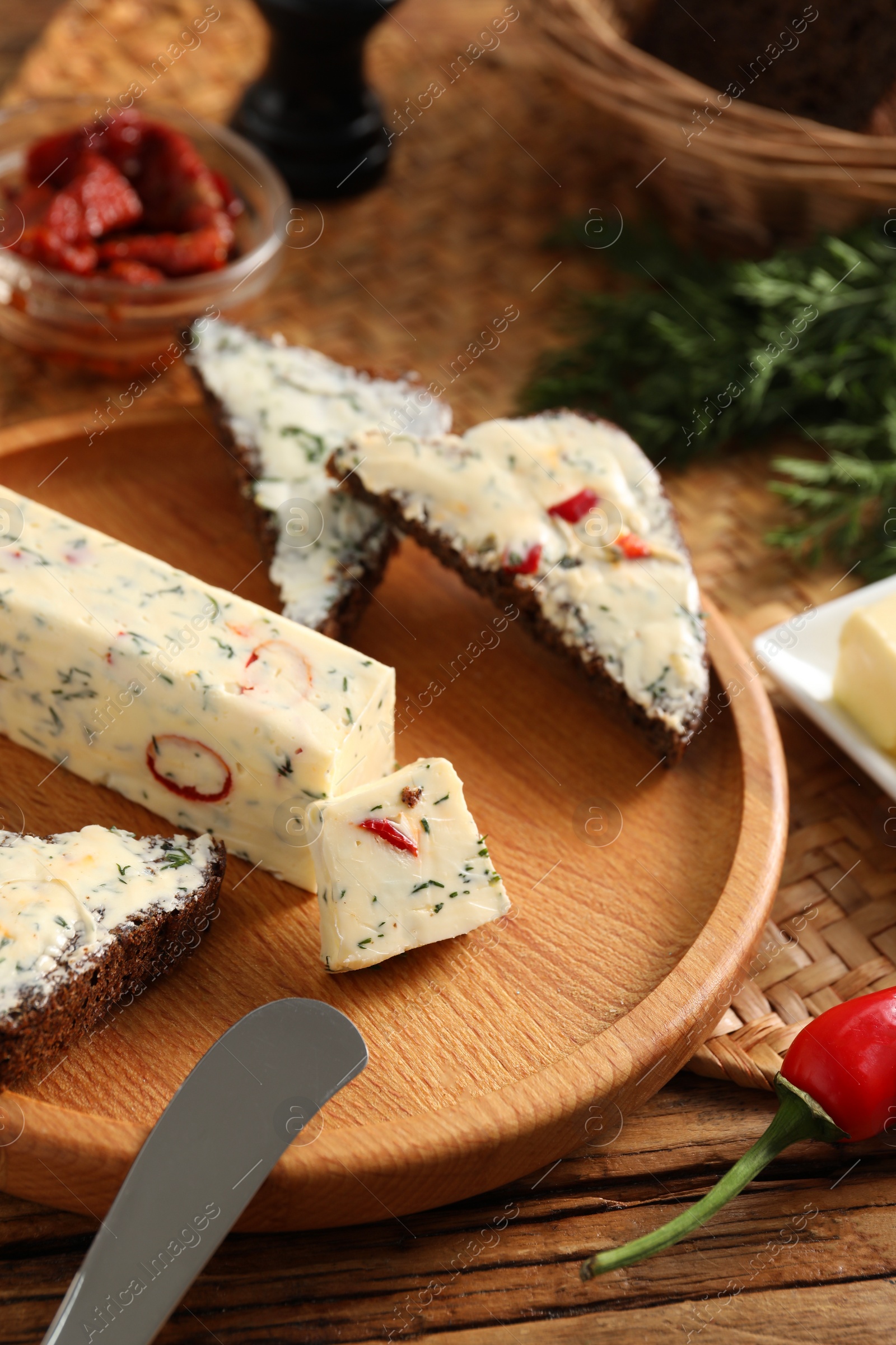 Photo of Tasty butter, dill, chili pepper and rye bread on wooden table