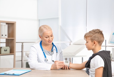 Doctor checking little boy's pulse with medical device in hospital