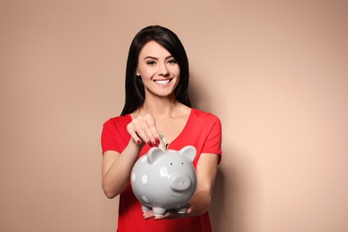 Photo of Beautiful woman putting money into piggy bank on color background