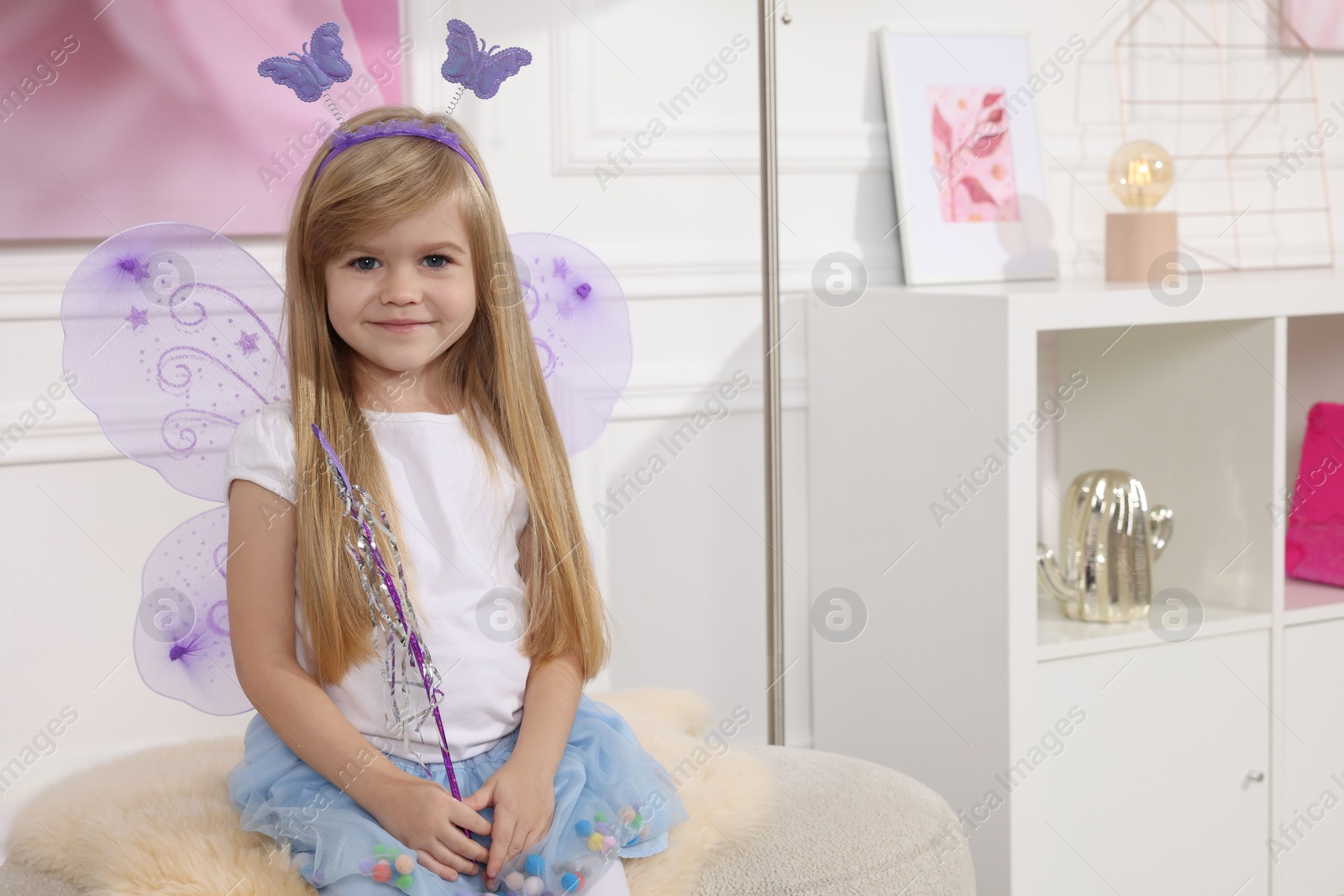 Photo of Cute little girl in fairy costume with violet wings and magic wand at home, space for text