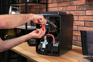 Photo of Repairman with screwdriver fixing coffee machine at table indoors, closeup