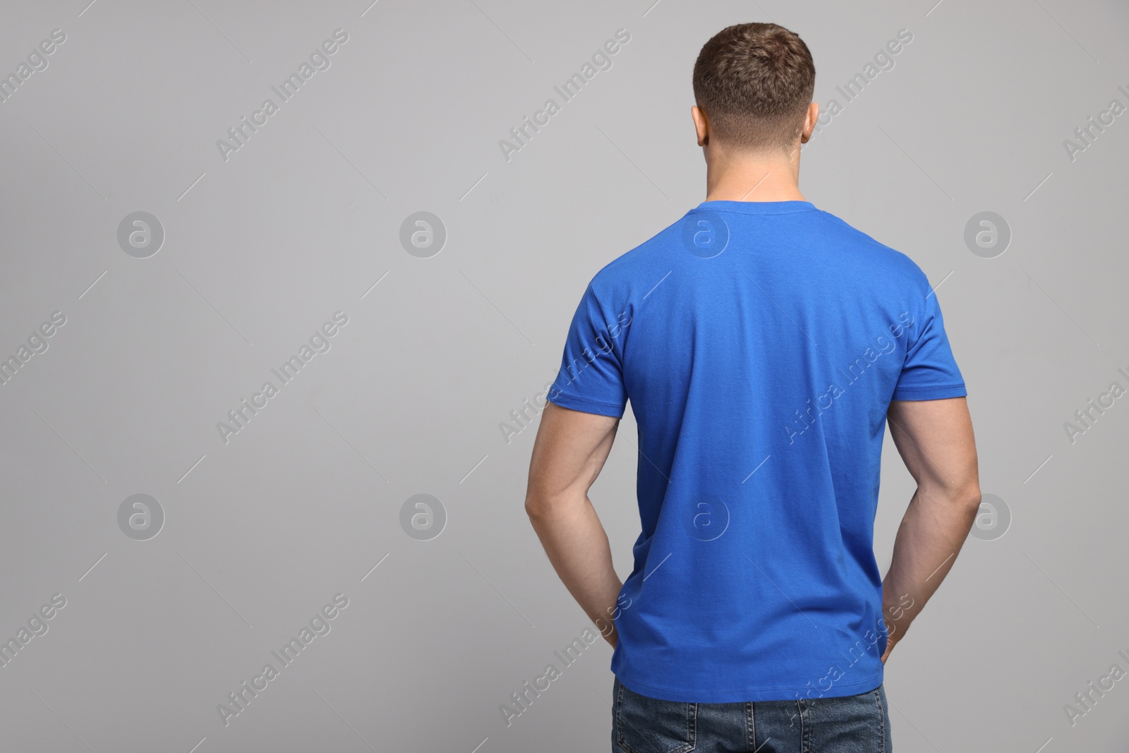 Photo of Man wearing blue t-shirt on light grey background, back view. Mockup for design