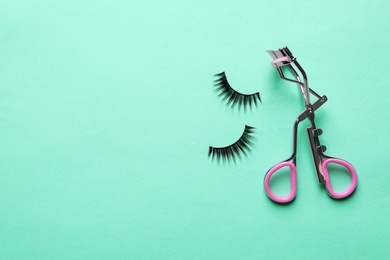 Photo of False eyelashes and curler on turquoise background, flat lay. Space for text