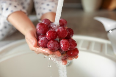 Woman washing fresh grapes in kitchen sink, closeup