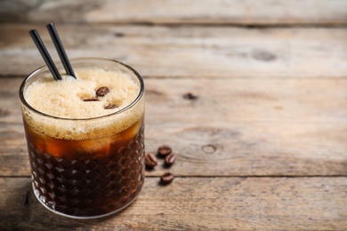 Photo of Glass of tasty refreshing cocktail with coffee beans on wooden table. Space for text