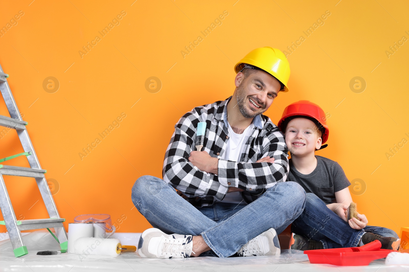Photo of Father and son with repair tools near orange wall