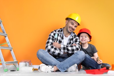 Father and son with repair tools near orange wall