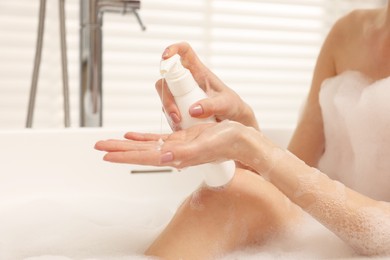 Woman applying shower gel onto hand in bath indoors, closeup